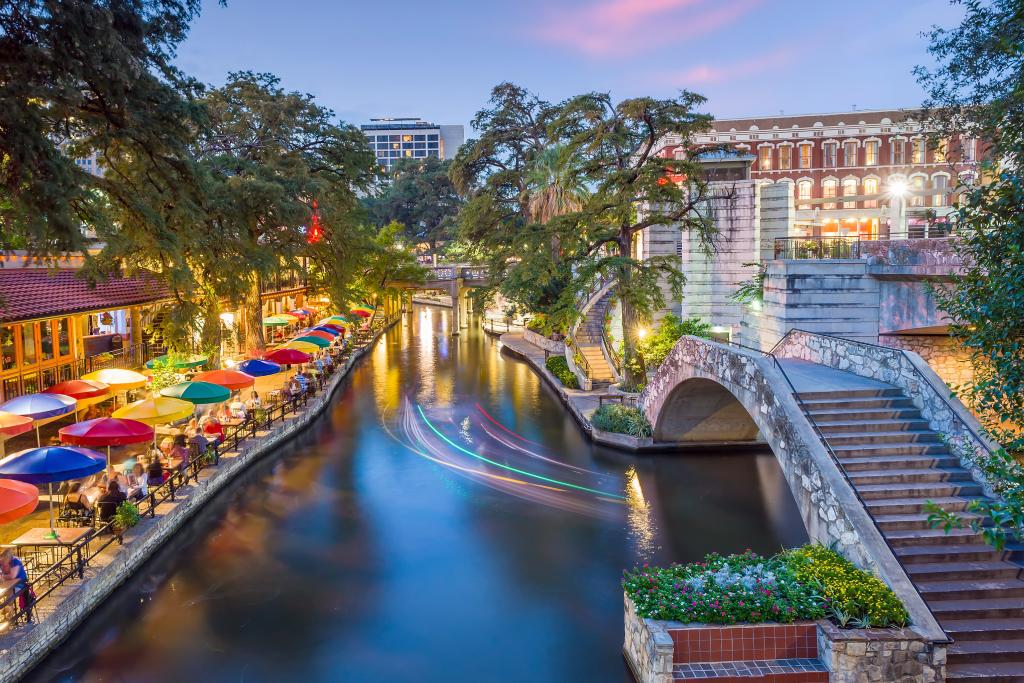 Scenic shot of the San Antonio River Walk at dusk with colorful umbrellas and water reflections.
